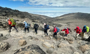 Climbers ascending a rocky section on Mount Kilimanjaro, highlighting the technical difficulty and route comparison – illustrating how hard is to climb Mount Kilimanjaro