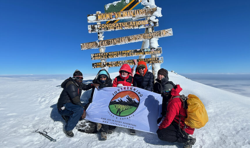 Students arrive at Uhuru Peak, 19,391ft. Holding a JoyTrekking Tours & Safari flag
