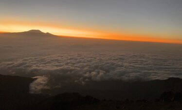Sunrise from Mount Meru summit with Mount Kilimanjaro silhouetted above a sea of clouds, Arusha National Park, Tanzania