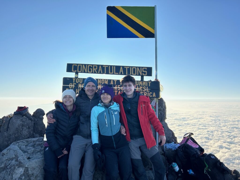 A joyful family celebrating at the Mount Meru summit in Arusha National Park, Tanzania, guided by local experts with stunning sunrise views.