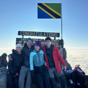 A joyful family celebrating at the Mount Meru summit in Arusha National Park, Tanzania, guided by local experts with stunning sunrise views.