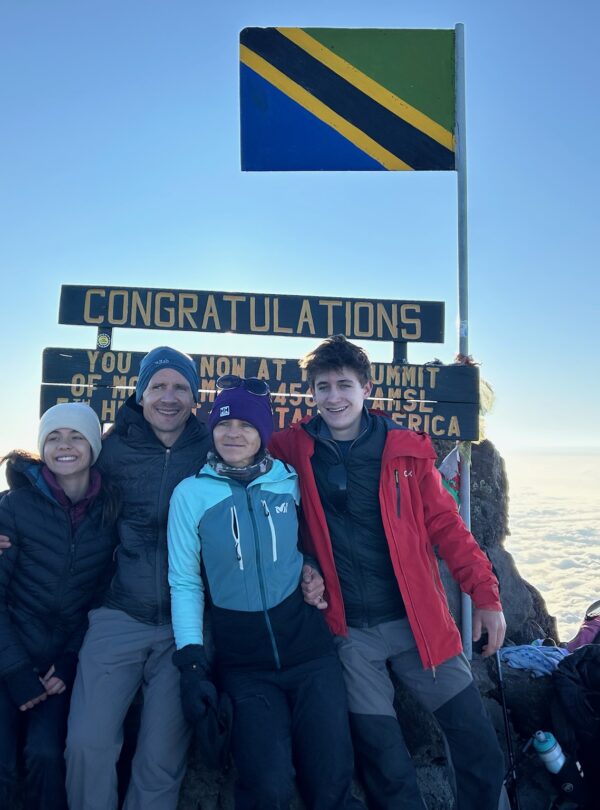 A joyful family celebrating at the Mount Meru summit in Arusha National Park, Tanzania, guided by local experts with stunning sunrise views.