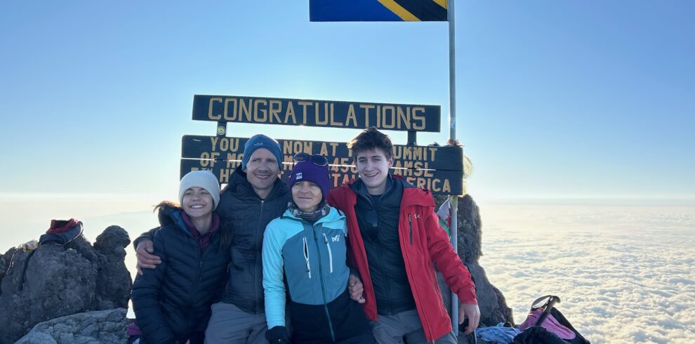 A joyful family celebrating at the Mount Meru summit in Arusha National Park, Tanzania, guided by local experts with stunning sunrise views.