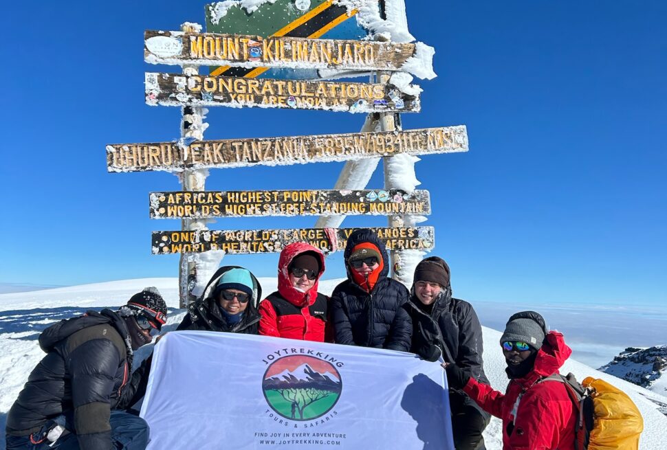 Group of climbers celebrating at Uhuru Peak on Mount Kilimanjaro after a successful summit using the right Mount Kilimanjaro Packing List for extreme high-altitude trekking
