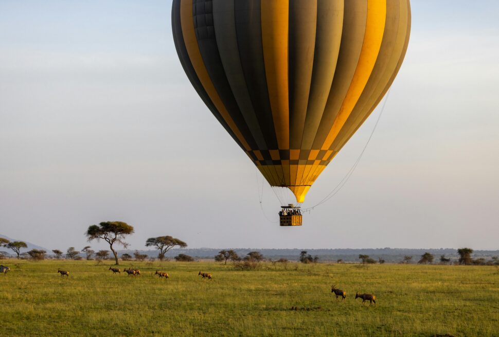 Hot Air Balloon Safari in Serengeti flying above the savannah with tourists enjoying a sunrise wildlife adventure.
