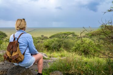 Tanzania sole female travel guide sitting on rocks inside national park during safari