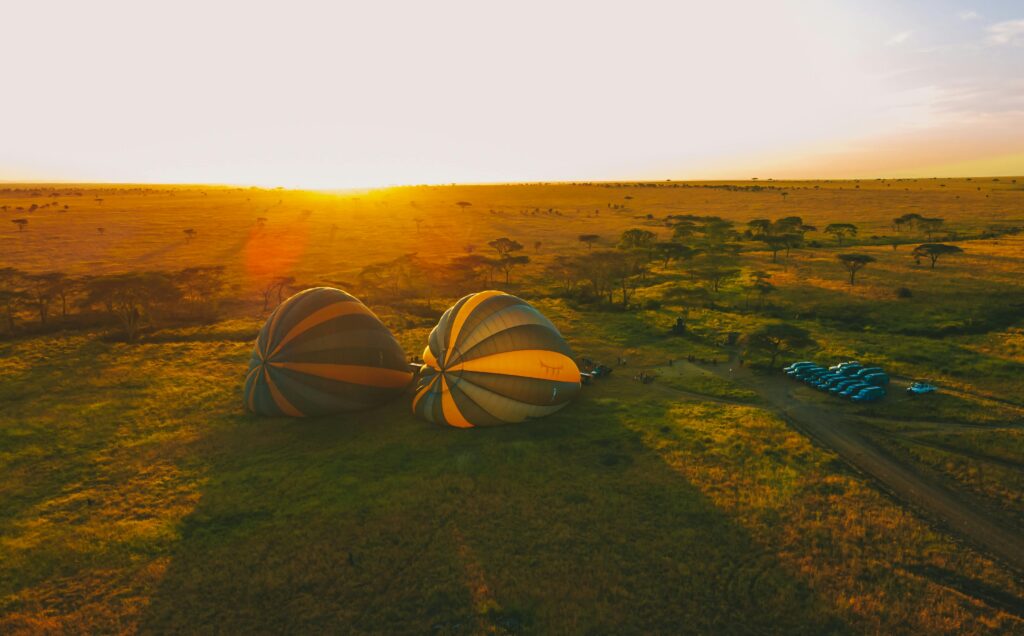 Two Hot Air Balloon Safari in Serengeti flying low over savannah plains during golden sunrise with sun rising in the background.