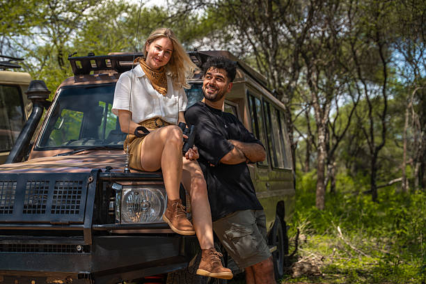 Young couple enjoying a Tanzania Safari for Couples next to a safari vehicle during a wildlife adventure