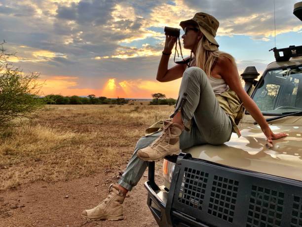 Woman wearing essential safari clothing standing on safari vehicle during Tanzania sunset game drive