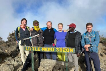Mount Meru trekking guide group of four tourists with professional guide standing at Little Meru summit during Tanzania trekking adventure