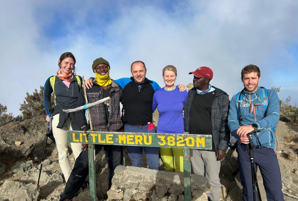 Mount Meru trekking guide group of four tourists with professional guide standing at Little Meru summit during Tanzania trekking adventure