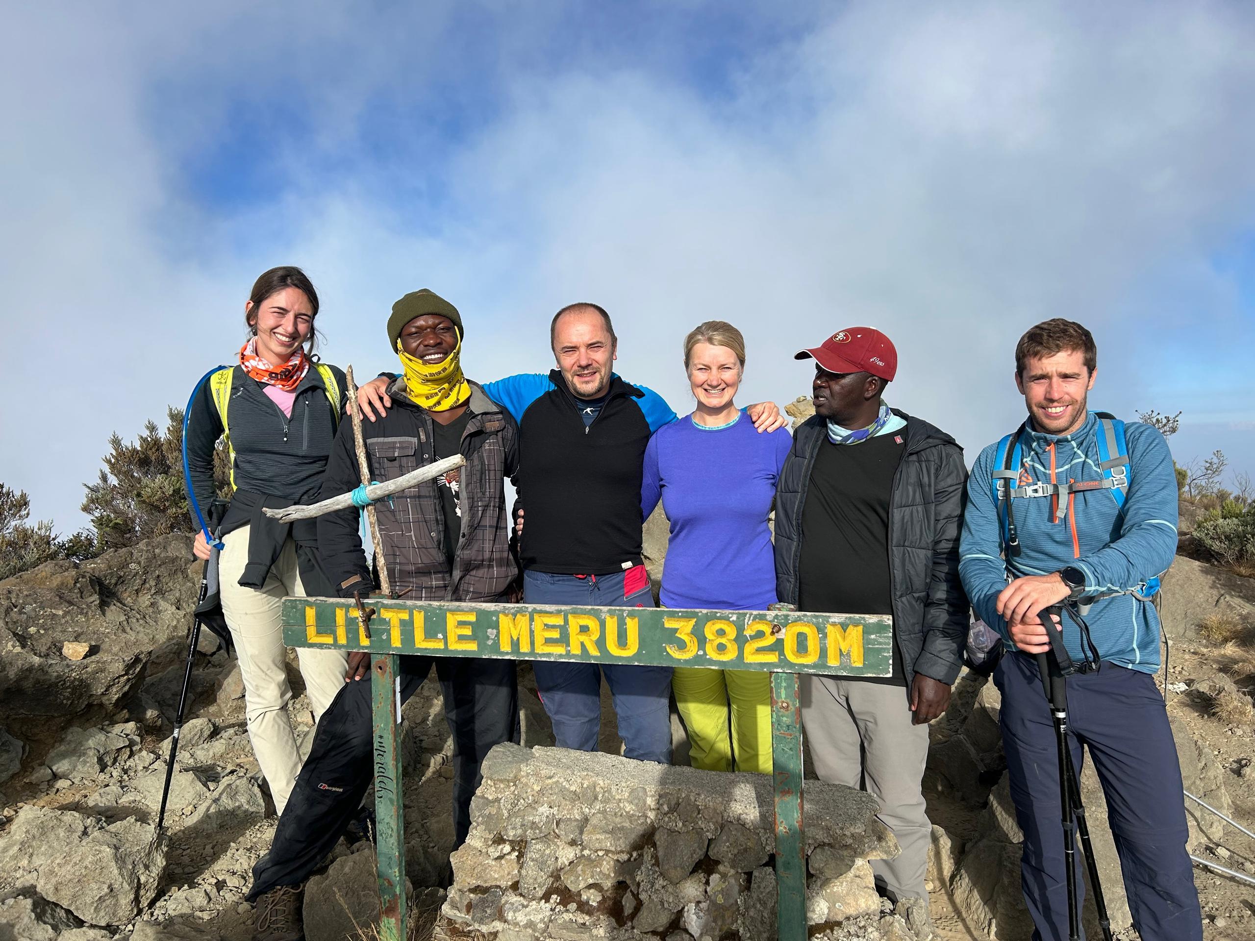 Mount Meru trekking guide group of four tourists with professional guide standing at Little Meru summit during Tanzania trekking adventure