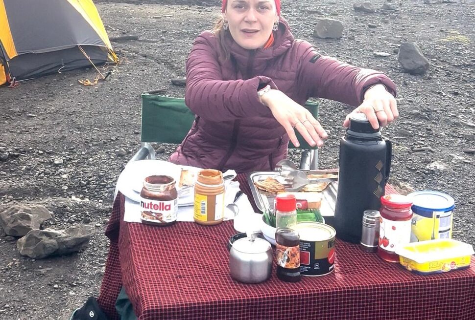French climber Pauline having breakfast at Shira Cave Camp on Mount Kilimanjaro, enjoying high-energy food as part of what to eat and drink on Mount Kilimanjaro for altitude performance.
