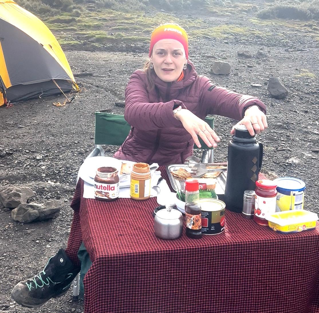 French climber Pauline having breakfast at Shira Cave Camp on Mount Kilimanjaro, enjoying high-energy food as part of what to eat and drink on Mount Kilimanjaro for altitude performance.