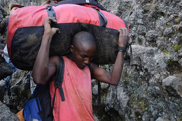 Porter carrying supplies and food on rocky trail to Mount Kilimanjaro summit in Tanzania illustrating weather awareness and emergency preparedness for Kilimanjaro Safety Essentials