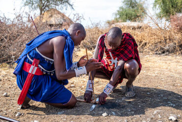 Maasai men demonstrating traditional fire-making during a Maasai cultural experience in Tanzania near Arusha