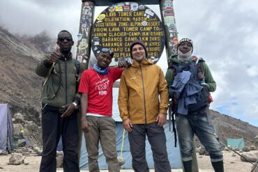 Kilimanjaro Climbing Costs 2026 porter team with guide January Mziray and international traveler at Lava Tower sign during Mount Kilimanjaro trek