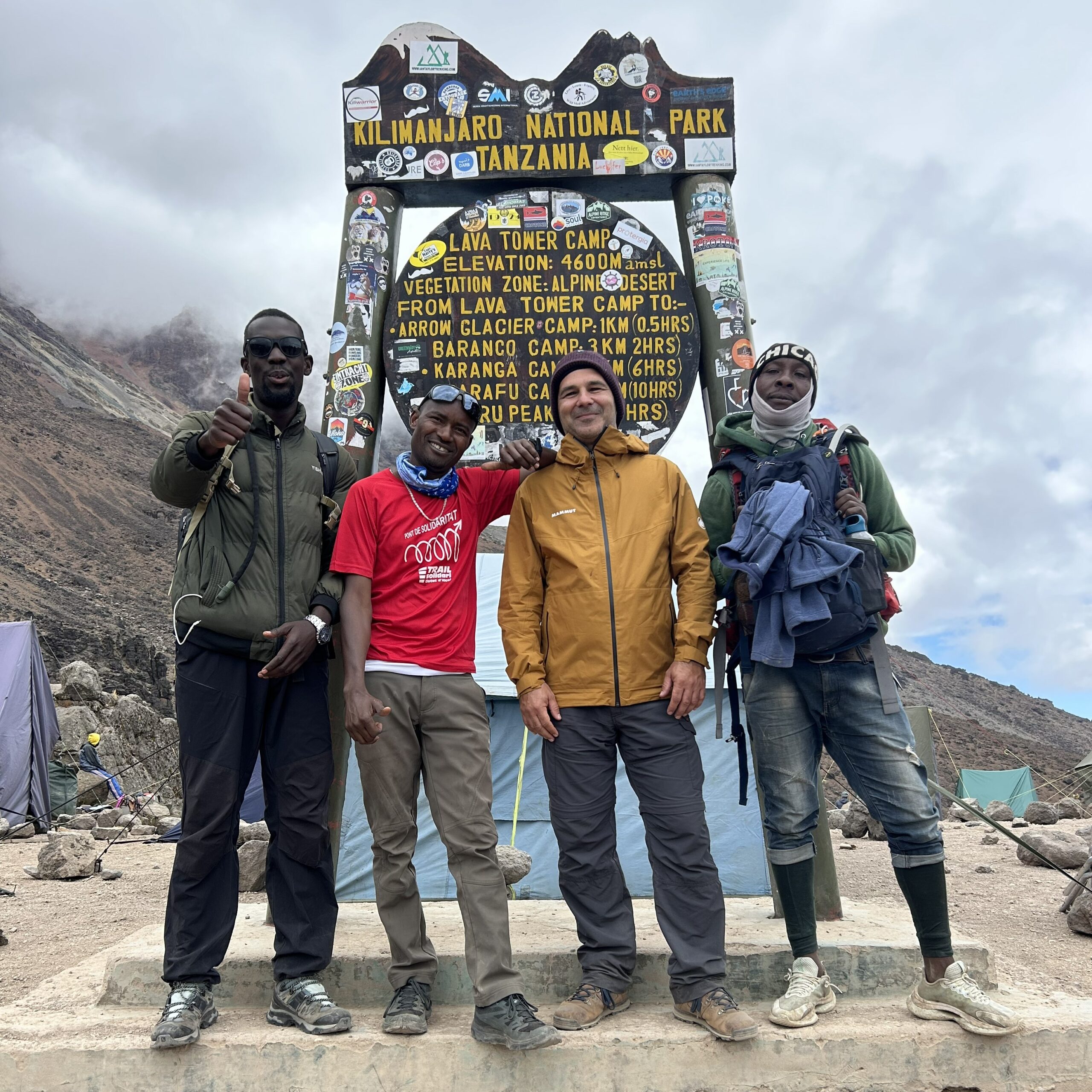 Kilimanjaro Climbing Costs 2026 porter team with guide January Mziray and international traveler at Lava Tower sign during Mount Kilimanjaro trek