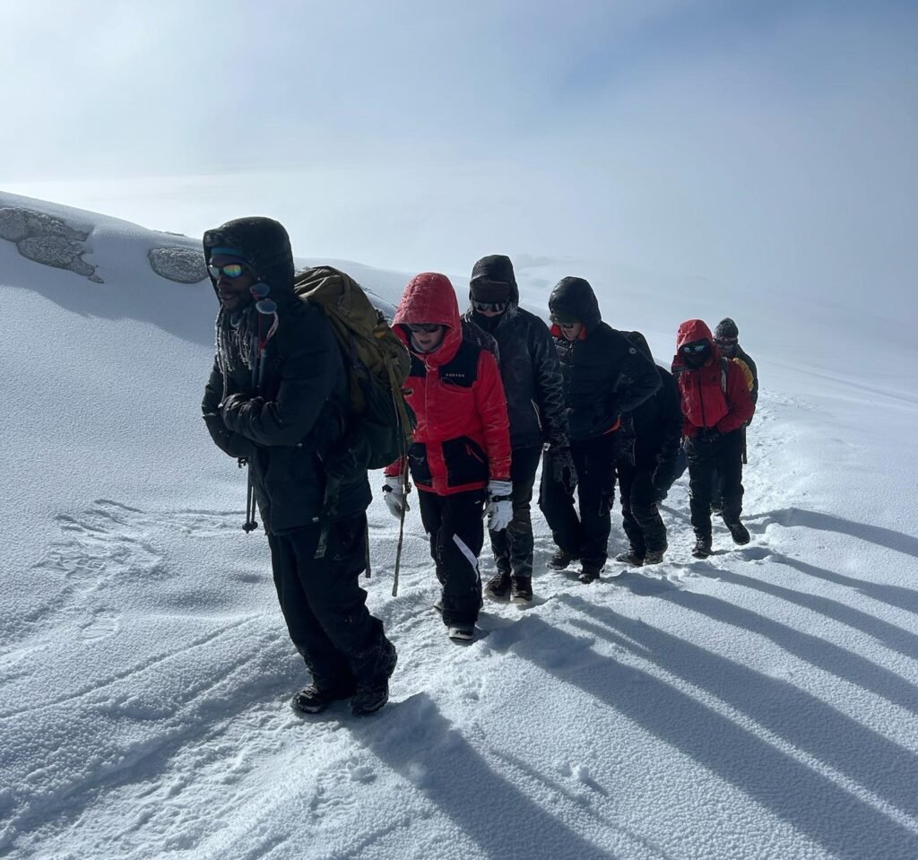 How many days to climb Mount Kilimanjaro — trekkers hiking through the snowy summit trail near Uhuru Peak in Tanzania