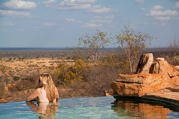 Blonde international traveler enjoying views of the African savannah from a luxury safari lodge infinity pool in Tanzania, representing Tanzania Luxury Safari experience