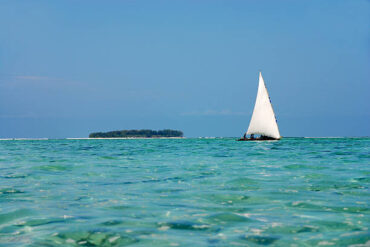 Mnemba Island Tours Zanzibar boat cruising on crystal clear Indian Ocean waters near Mnemba Island with turquoise ocean view and scenic marine landscape
