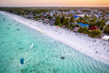 Kitesurfing at Paje Beach in Zanzibar during sunset over turquoise Indian Ocean waters with tourists enjoying vibrant beach activities