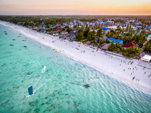 Kitesurfing at Paje Beach in Zanzibar during sunset over turquoise Indian Ocean waters with tourists enjoying vibrant beach activities