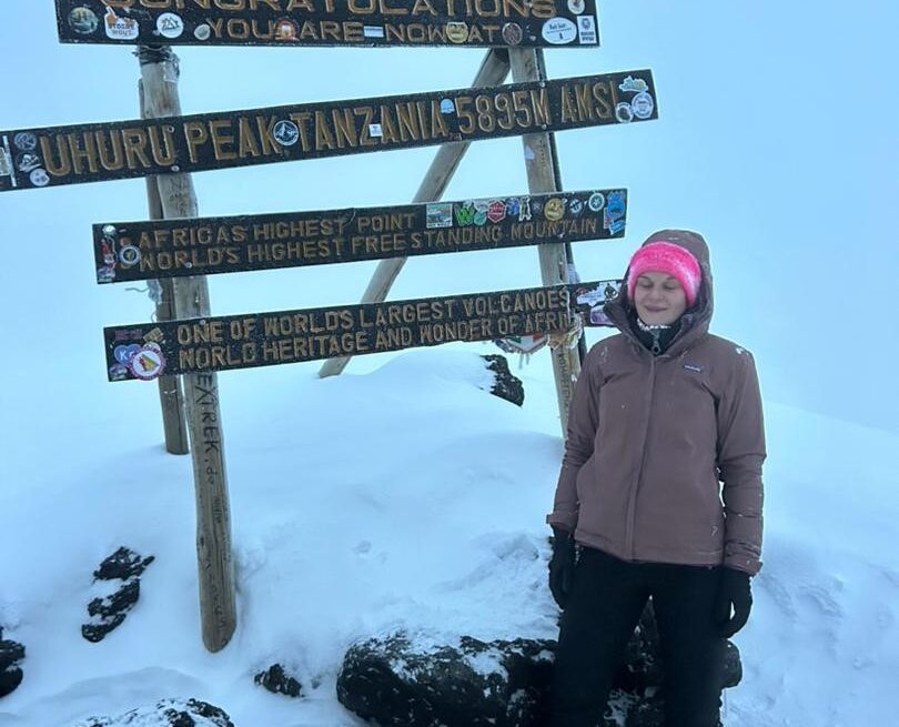 Pauline standing at Uhuru Peak on Mount Kilimanjaro covered in snow after summit, showing achievement despite altitude sickness Altitude Sickness on Mount Kilimanjaro challenges