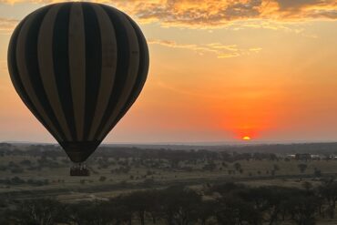 Best Sunset Spots in Tanzania showing Serengeti National Park landscape with hot air balloon floating above the savannah during a golden sunset