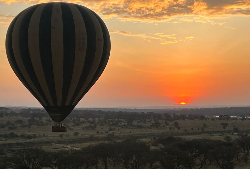 Best Sunset Spots in Tanzania showing Serengeti National Park landscape with hot air balloon floating above the savannah during a golden sunset