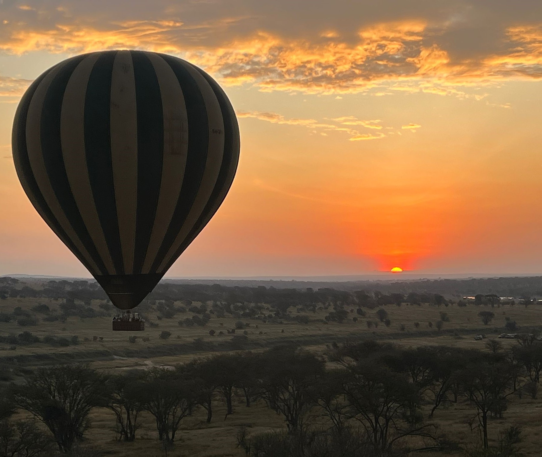 Best Sunset Spots in Tanzania showing Serengeti National Park landscape with hot air balloon floating above the savannah during a golden sunset