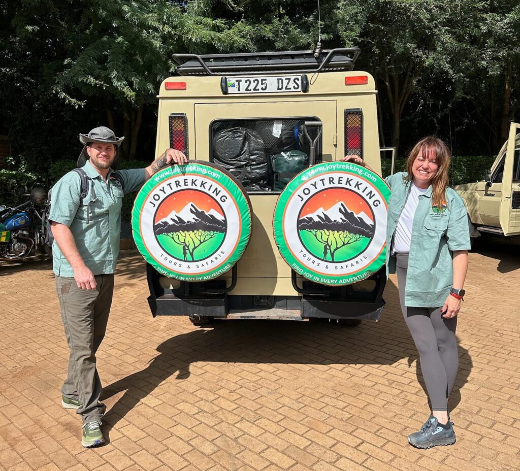 Happy couple on luxury safari in Tanzania posing behind JoyTrekking Tours & Safaris vehicle