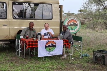 Affordable Tanzania Safari Packages experience showing international traveler with JoyTrekking Tours guide and driver enjoying a refreshment break in the African savannah during a wildlife safari in Tanzania
