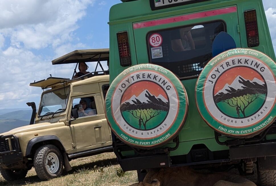 Safari Jeep Tanzania Tours showing two lions resting behind a safari jeep in Serengeti during a wildlife adventure