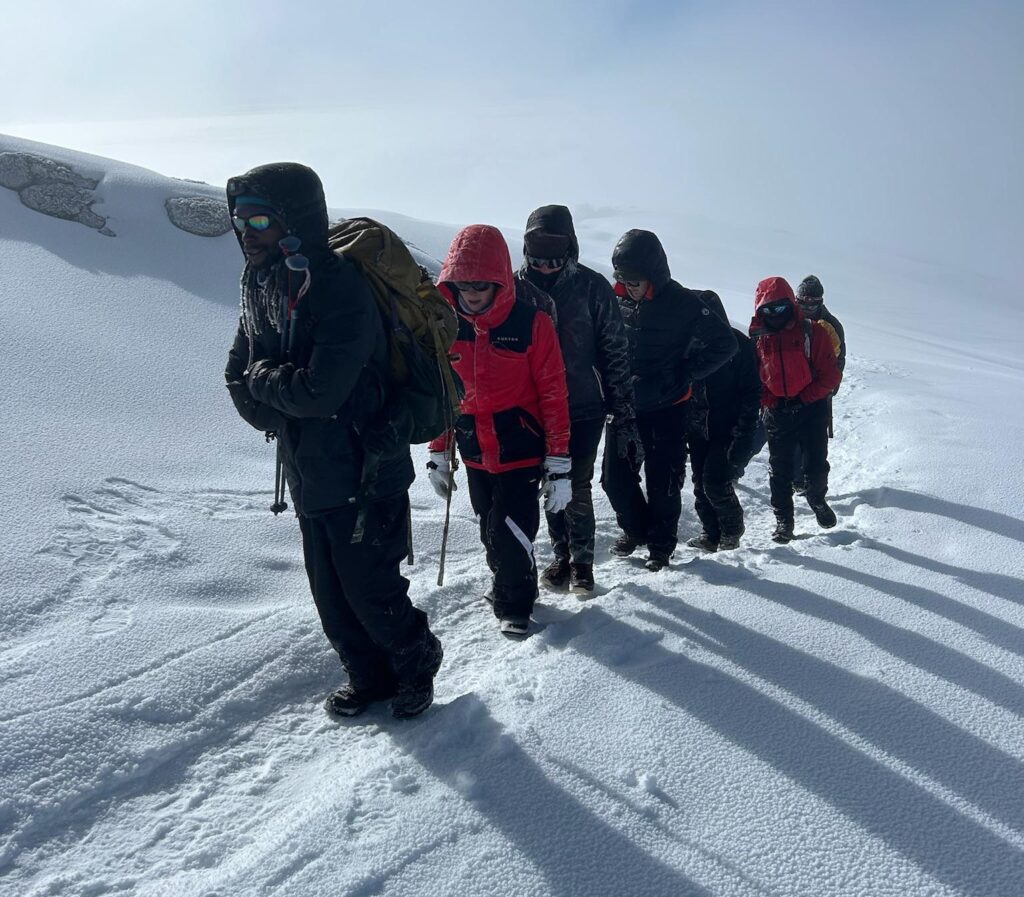 International travellers climbing Mount Kilimanjaro through snowy conditions during a mentally challenging summit trek in Tanzania