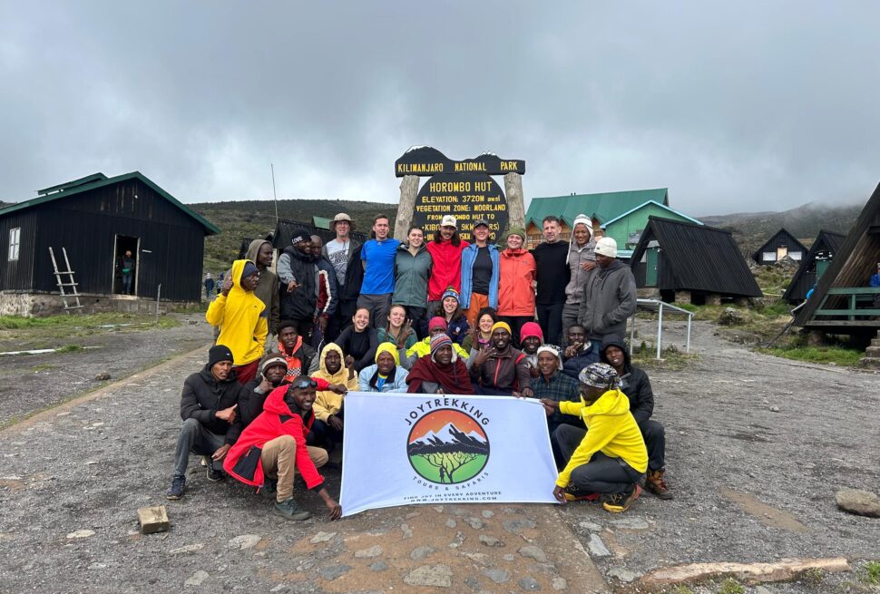 Best Kilimanjaro trekking company crew of travelers, guides, and porters with JoyTrekking Tours & Safaris flag at Horombo Hut on Mount Kilimanjaro