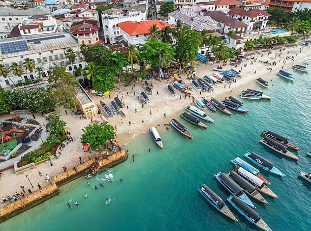 Zanzibar Marine Activities Cost guide featuring Stone Town waterfront with traditional dhow boats, turquoise ocean, and visitors enjoying the beach