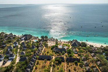 Royal Zanzibar Beach Resort: Nungwi beachfront resort in Zanzibar with traditional bungalows, pools and sun loungers opening onto turquoise Indian Ocean waters dotted with boats under a bright sky